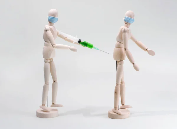 The concept of vaccination or injections for protection from viruses and bacteria. A wooden model of a masked man vaccinates a green vaccine to another wooden person. neutral background. buttock injection