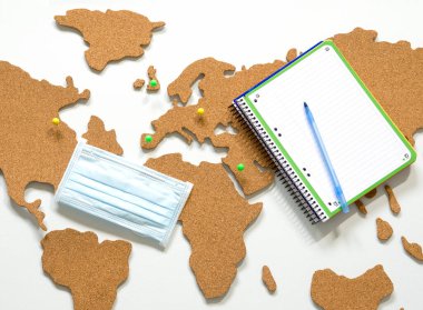 Bir salgın sırasında seyahat kavramı, bir dünya haritası ve kişisel koruma aracı olarak maske, tarafsız arka planda düz yatıyordu,