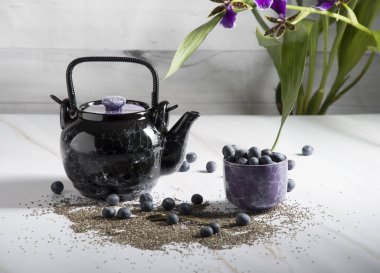 Siyah seramik bir çaydanlık ve hafif bir arka planda Chia tohumları, yoğurt ve yaban mersinli bir tatlıyla bir orkide