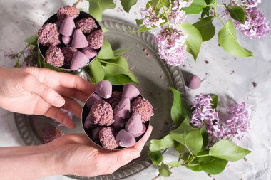 Belgian sweets cuberdon and pralines in silver glasses, spring still life with lilac flowers, flat lay with female hands