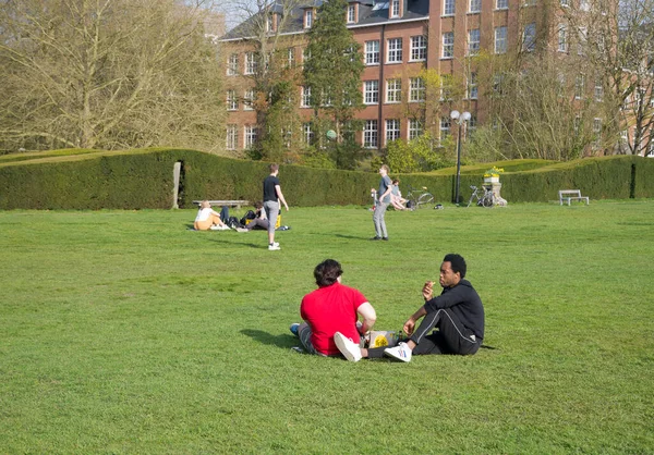 Groep van gemengde race vrienden ontspannen samen op het gazon in de buurt van kasteel Arenberg, concept Sociale afstand, Leuven, België, 1 april 2021. — Stockfoto