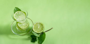Nane ve limonlu çay, sakinleştirici etkisi olan yeşil renkli, yeşil arka planda yakın plan, üst manzara. Mojito, sağlık içeceği, alternatif tıp
