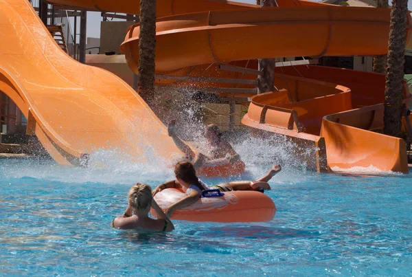 Gyerekek és nők úsznak és csúsznak le a medencén a hotel vízi parkjában. — Stock Fotó