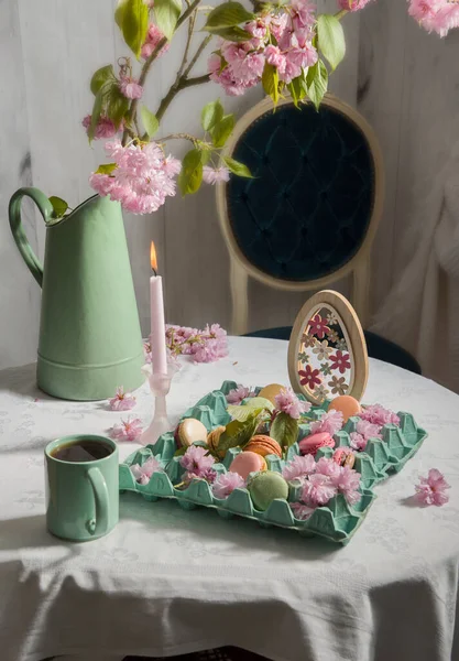 Colored macarons on the table against the background of blooming sakura and a cup of coffee, Easter still life — Stock Photo, Image
