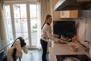 Genç kadın gülümserken, mutfak tezgahını bezle silerken, modern dairesini düzenli, hijyenik ve rahat tutmak için günlük temizlik işleri yapıyor.