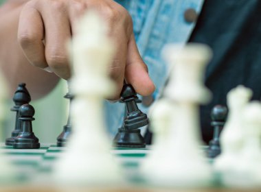 Yeşil tahtada satranç oyunu, bir el siyah bir piyonu tutar.