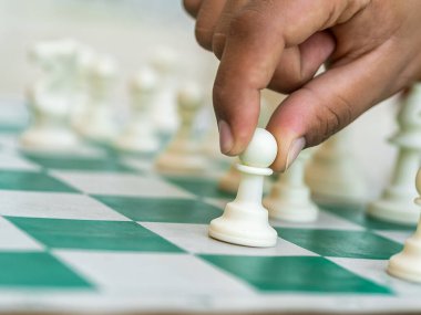 Yeşil tahtada satranç oyunu, bir el beyaz bir piyonu tutar