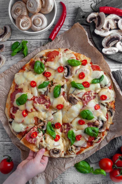 Sosisli, mantarlı ve peynirli pizza ahşap gri arka planda, bir parçası bir çocuğun eliyle çekiliyor.