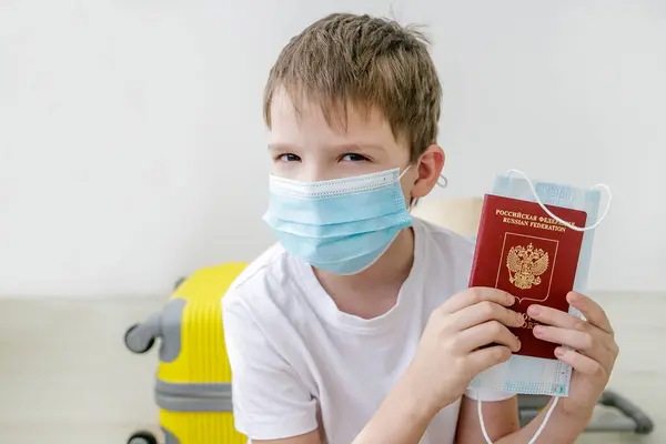 Tıbbi maskeli ve uluslararası pasaportlu bir çocuk seyahat etmek için bekliyor..