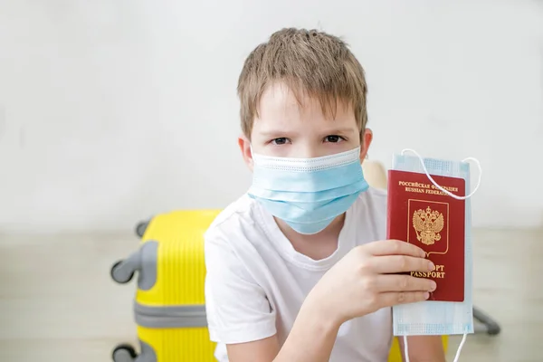 Tıbbi maskeli ve uluslararası pasaportlu bir çocuk seyahat etmek için bekliyor..