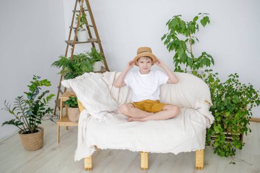 Bir çocuk, bir çocuk evin yanındaki kanepede oturur ve bir şapka takar..