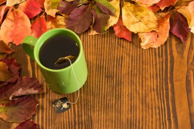 sonbahar yaprakları ve ahşap arka plan üzerinde çay bardağı