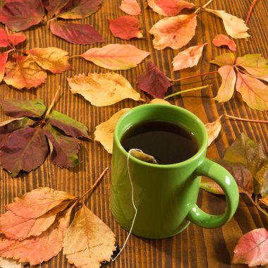 sonbahar yaprakları ve ahşap arka plan üzerinde çay bardağı