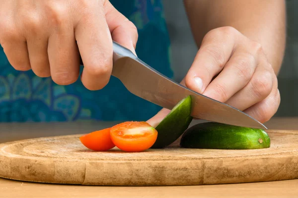 Manos rebanando pepino y tomate en la tabla de cortar — Foto de Stock