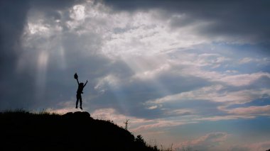 Bir oğlan dağda günbatımında atlıyor