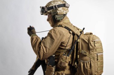 Taktik ekipman ve üniformalı erkek asker (çakal kahverengi renk). Stüdyoda beyaz bir arkaplanda çekilmiş.
