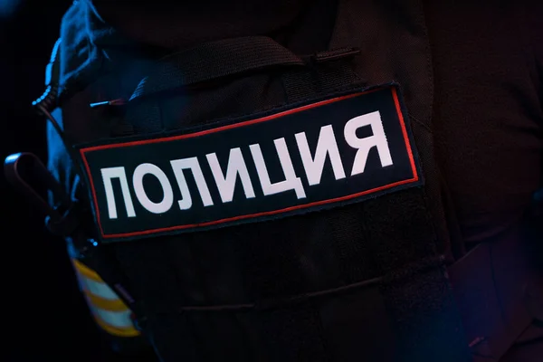 Male in black uniform conforms to Police SWAT. Patch on the back with the inscription Police in Russian. Black background (red and blue lights)