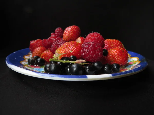 Различные ягоды на тарелке на черном фоне . — стоковое фото