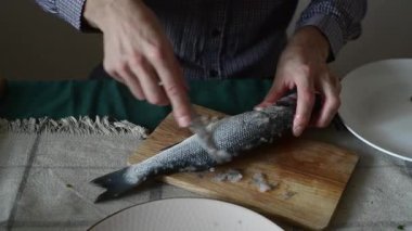 Bir adam balık pullarını bıçakla temizler.