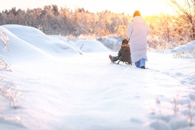 Genç bir anne, oğlunu gün batımına karşı karlı bir alanda kızakla kaymaya götürür. Kış, annelik ve kış aktiviteleri kavramı..
