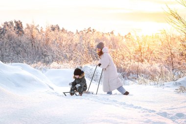Genç bir anne, oğlunu gün batımına karşı karlı bir alanda kızakla kaymaya götürür. Kış, annelik ve kış aktiviteleri kavramı..