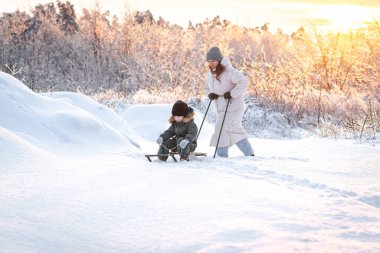 Genç bir anne, oğlunu gün batımına karşı karlı bir alanda kızakla kaymaya götürür. Kış, annelik ve kış aktiviteleri kavramı..