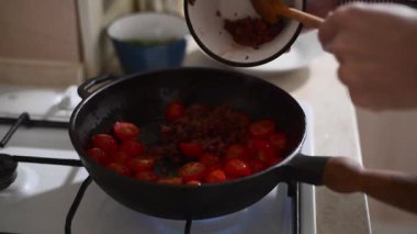 Taze maydanozlu ve zeytinli tavada kızaran vişneli domatesleri yakından izleyin. Adam fırında sebze pişiriyor, evde sağlıklı bir Akdeniz yemeği hazırlıyor. Taze malzemelerle doğal gıda hazırlama süreci.