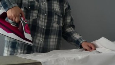 Kadın ellerinin ütüden su sıkarken tahtadaki kıyafetleri ütülediği yan görüntü. Evde bakım sırasında pürüzsüz kumaşa nemli uygulama gösteren ev çamaşırları..