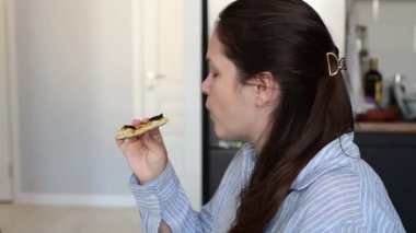 Ev mutfağında peynirli ve mantarlı klasik Napoli pizzası yiyen bir kadın. Rahat bir yemek sırasında geleneksel İtalyan yemeklerini gösteren sıradan bir yemek sahnesi..