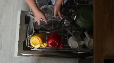 Kadının bulaşık makinesini açması, üst rafı çıkarması ve temiz mutfak aletlerini çıkarması. Üst mutfak rutini evde ısıya dayanıklı aletlerin boşaltıldığını gösteriyor.