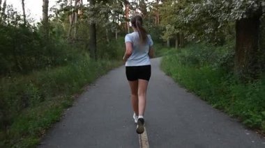 Young woman running away from camera on park pathway in slow motion. Tracking follow shot creates dynamic depth and motivational cinematic atmosphere. Ideal for fitness, endurance, and active lifestyle concepts.