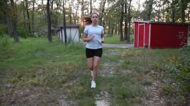 Gün batımında çamur parkında kameraya doğru ağır çekimde koşan genç bir kadın. Sıcak altın arkaplan ışığıyla ön izleme hareketi dinamik ve ilham verici bir atmosfer yaratır. Fitness, dayanıklılık ve sağlıklı yaşam tarzı kavramları için idealdir..