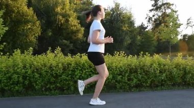 Genç kadın yavaş çekimde gün batımına doğru kaldırımda koşuyor. Altın parıltıyla dolu yan izleme çekimi sinematik ve ilham verici kentsel fitness atmosferi yaratır. Motivasyon, özgürlük ve aktif yaşam tarzı kavramları için ideal.