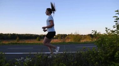 Ağır çekimde kaldırım kenarında koşan genç bir kadın ön plandaki çalıların arasından film çekiyor. Yan izleme çekimi sinematik kentsel atmosfer için ön, orta ve arka plan elementlerine sahip katmanlı derinlik yaratır.