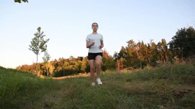 Genç bir kadın çamur parkında kameraya doğru koşuyor. Gün batımının sıcacık ışığıyla aydınlatılıyor. Düşük açılı yavaş çekim güçlü ve sinematik zindelik atmosferi yaratır. Motivasyon, dayanıklılık ve aktif yaşam tarzı kavramları için ideal.