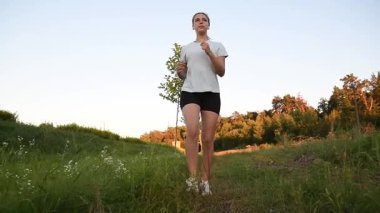 Genç bir kadın çamur parkında kameraya doğru koşuyor. Gün batımının sıcacık ışığıyla aydınlatılıyor. Düşük açılı yavaş çekim güçlü ve sinematik zindelik atmosferi yaratır. Motivasyon, dayanıklılık ve aktif yaşam tarzı kavramları için ideal.