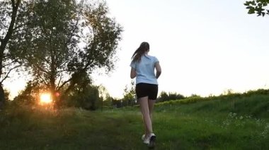 Genç bir kadın çamur parkında gün batımına doğru koşuyor. Çim seviyesinin yakınından çekilmiş. Yavaş çekim geri izleme çekimi güçlü bir sinematik derinlik ve ilham verici bir atmosfer yaratır. Motivasyon, dayanıklılık, kişisel büyüme kavramları için ideal.