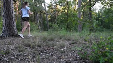 Yavaş çekimde ormanda koşan genç bir kadın statik çerçeveden geçiyor. Doğal ortam dinamik ve enerjik bir atmosfer yaratır. Fitness, dayanıklılık ve aktif yaşam tarzı kavramları için ideal.