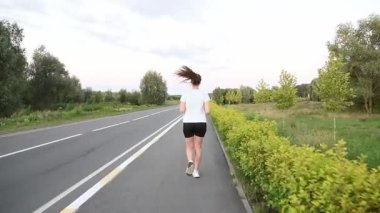 Gerçek zamanlı olarak kaldırım kenarında kameradan kaçan genç bir kadın. Arka plan izleme çekimi doğal hareketi ve dinamik kentsel zindelik atmosferini yakalar. Dayanıklılık, ilerleme ve aktif yaşam tarzı kavramları için ideal.