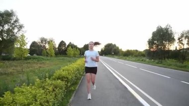 Gerçek zamanlı olarak kaldırım kenarında kameraya doğru koşan genç bir kadın. Ön izleme çekimi doğal hareketlerle dinamik kentsel zindelik atmosferi yaratır. Dayanıklılık, performans ve aktif yaşam tarzı kavramları için ideal.