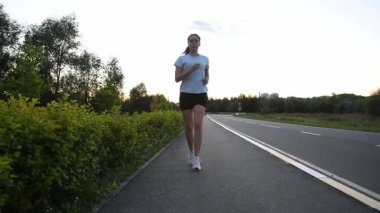 Yol kenarında çömelmiş genç bir kadın gerçek zamanlı olarak ayağa kalkıp kameraya doğru koşuyor. İzleme çekimi doğal hareketi ve dinamik kentsel zindelik atmosferini yakalar. Yeni başlangıçlar, motivasyon ve aktif yaşam tarzı kavramları için ideal.