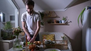 Adam yatakta kahvaltı için kruvasan hazırlıyor, onları mutfak masasında taze marul yapraklarıyla dolduruyor. Düşünceli bir ev yemeği ve özenli bir jest gösteren rahat bir sabah yaşam tarzı sahnesi..