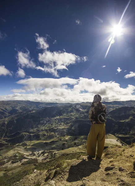 Menina de pé em uma colina olhando para montanhas contra o sol — Fotografia de Stock