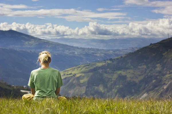 Szőke lány ül a fűben, és szeretnének hegyek, meditáció — Stock Fotó