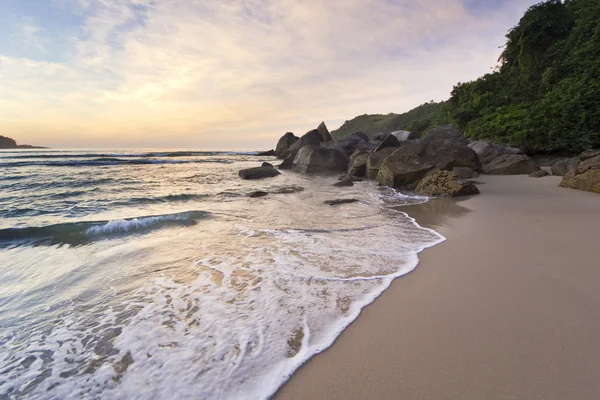Roxo nascer do sol na praia tropical, ondas e pedras na costa — Fotografia de Stock