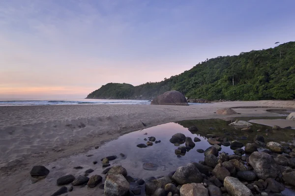 Roxo nascer do sol na praia tropical, ondas e pedras na costa — Fotografia de Stock