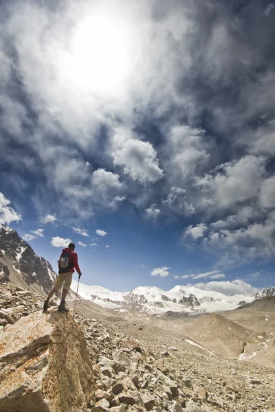 Hombre de pie en un acantilado en las montañas con postes — Foto de Stock