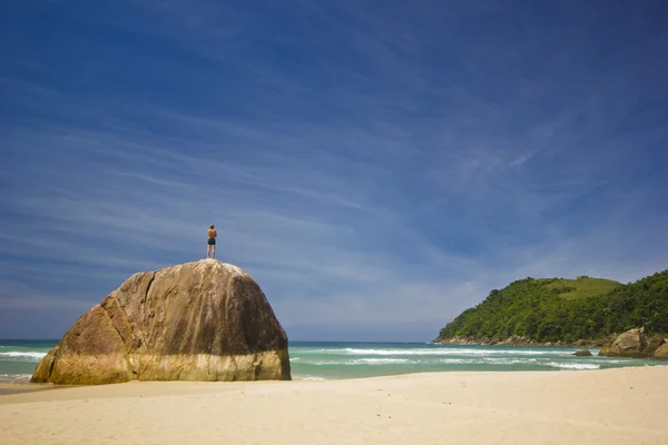 Homem de pé na grande pedra na praia tropical com montanhas — Fotografia de Stock