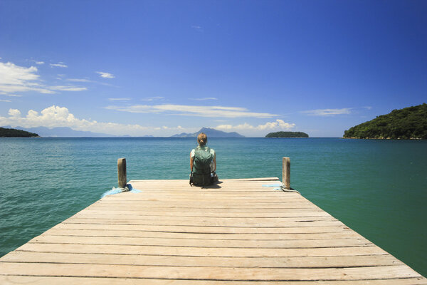 traveller sitting on pier in ocean beach with green water
