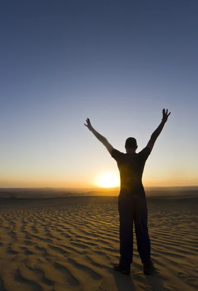 Homem de pé com as mãos para cima ao pôr do sol no deserto — Fotografia de Stock